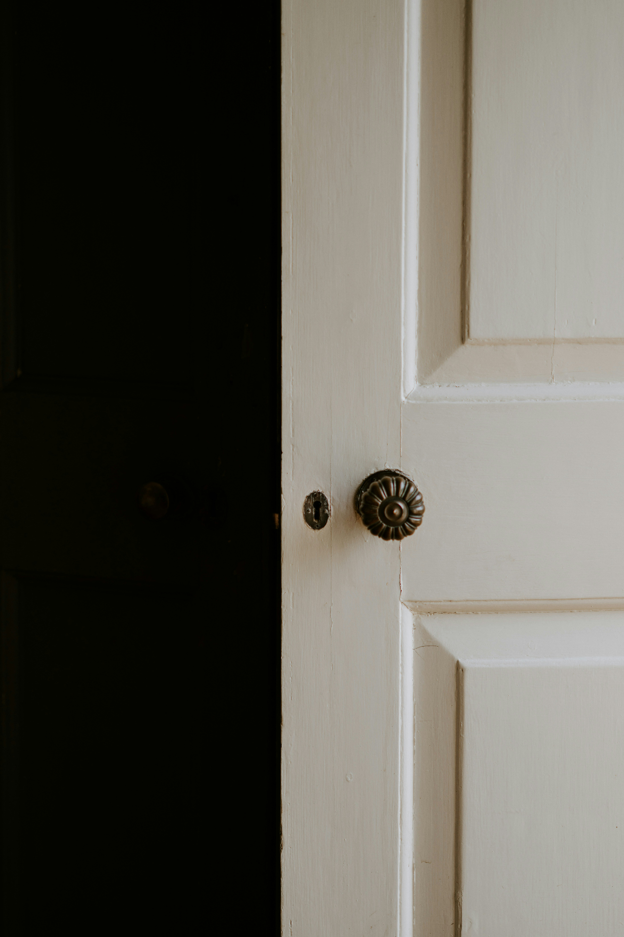 A white paneled interior door slightly ajar, showing a vintage brass doorknob.
